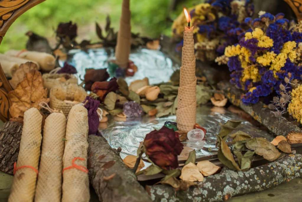 Beeswax candle burning on an altar surrounded by dried flowers, crystals, herbs, and ritual tools for intuitive or ancestral energy healing.